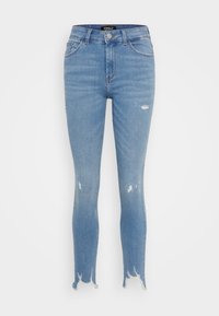 Jeans ajustados de color azul claro con dobladillos deshilachados y pequeños parches desgastados en las piernas, cintura de altura media y bolsillos frontales.
