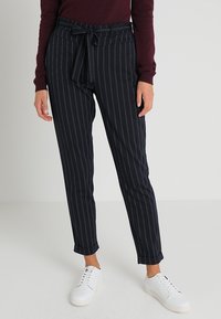 Granatowe spodnie w paski z elastycznym pasem, zwężające się nogawki i miękki materiał. Noszone z białymi trampkami, z podwiniętymi манжетą.