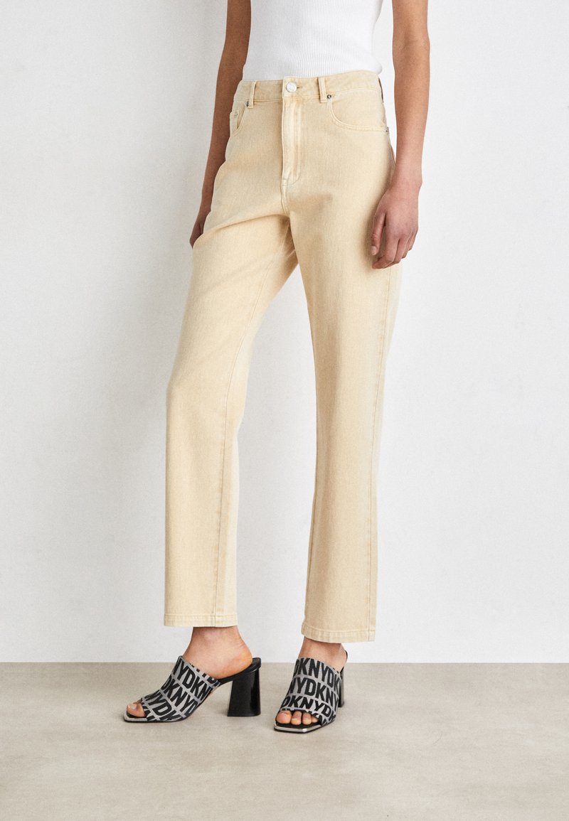 Jeans dritti color beige chiaro con vita alta, abbinati a mules nere open-toe con un motivo stampato e tacco a blocco.