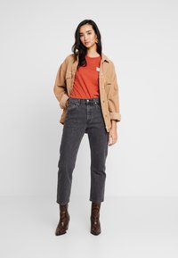 Brun manchestyg jacka över en orange skjorta, kombinerad med högmidjade svarta jeans och bruna stövlar i ormskinn.