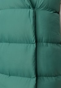 Gepolsterte grüne Weste mit glatter Textur, die genähte Abschnitte und eine vordere Knopfschließe aufweist. Leicht und strapazierfähig.