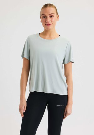 Helles graues kurzärmliges Sport-T-Shirt aus atmungsaktivem Material, mit rundem Ausschnitt und leicht geschwungenem Saum. Schwarze Leggings mit Logo.