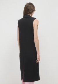 Schwarzes ärmelloses Kleid mit hohem Kragen, stromlinienförmigem Design, gerader Silhouette und einem Schlitz im Rücken, aus glattem Stoff gefertigt.