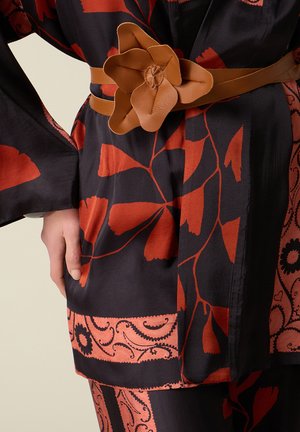 Czarna i czerwona sukienka w kwiatowy wzór z szerokimi rękawami, podkreślona beżowym skórzanym paskiem z dużą klamrą w kształcie kwiatka w talii.