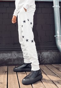 Ljusgråa mjukisbyxor med svarta stjärnmönster på sidan, kombinerade med svarta höga sneakers med mjuk läderstruktur.