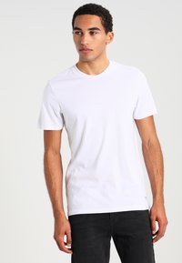 T-shirt bianco con maniche corte in morbido cotone, collo rotondo e design minimalista. Indossato con jeans scuri.