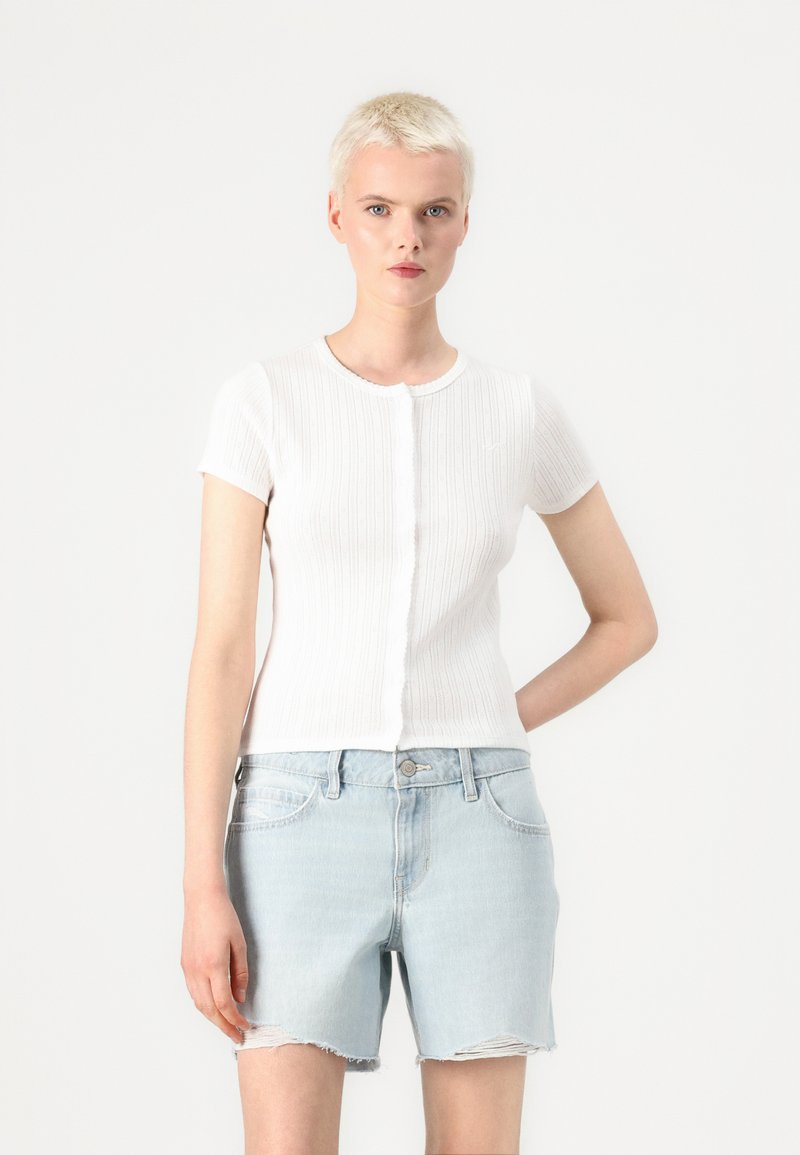 Biała, prążkowana koszulka na krótki rękaw, okrągły dekolt, z zapięciem na guziki z przodu. Połączona z jasnoniebieskimi, postrzępionymi szortami dżinsowymi.