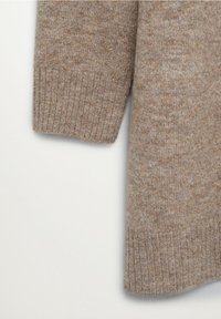 Beżowy sweter z dzianiny o textured powierzchni, z prążkowanymi mankietami i luźnym krojem, podkreślający miękki materiał i naturalne odcienie.