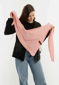 Roze gebreide sjal met een gestructureerd patroon, vastgehouden door een persoon, met een driehoekige vorm en accenthardware aan één kant.