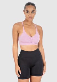 Vaaleanpunainen lyhyt urheilutoppi ohuilla olkaimilla ja rypytetyllä yksityiskohdalla, yhdistettynä korkeavyötäröisiin mustiin pyöräilyshortseihin, joissa on sileä pinta.