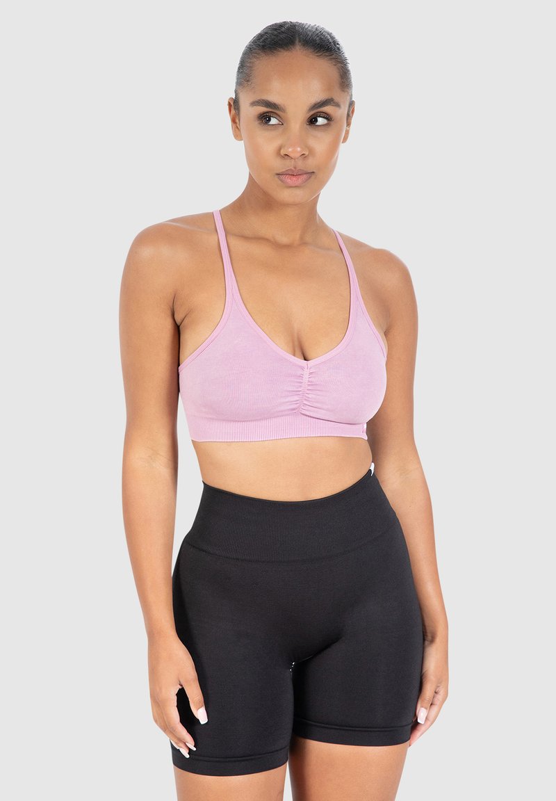 Vaaleanpunainen lyhyt urheilutoppi ohuilla olkaimilla ja rypytetyllä yksityiskohdalla, yhdistettynä korkeavyötäröisiin mustiin pyöräilyshortseihin, joissa on sileä pinta.