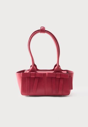 Červená kožená kabelka s dvoma hornými rúčkami, dekoratívnymi prednými mašľami a visačkou na boku na bielom pozadí.