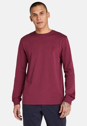 Camiseta de algodón burdeos de manga larga con cuello redondo, que presenta un pequeño logo rojo en el pecho y puños acanalados. Textura suave y corte recto.