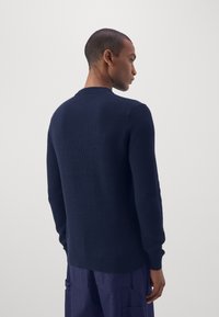 Marineblå striktrøje med rund halsudskæring, lange ærmer, ribbede manchetter og kant. Stoffet har en tekstureret overflade.