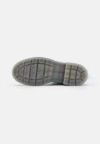 Semelle de chaussure en matériau caoutchouteux translucide avec un motif profond rainuré pour une meilleure adhérence et durabilité.