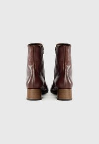 Brown leather ankle boots with a smooth texture, zippers on the back, and a stacked wooden heel. Simple and sleek design.