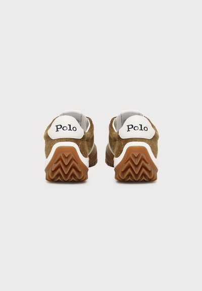 Paire de baskets en suède marron vue de l’arrière, talons blancs avec texte noir « Polo », semelles en caoutchouc beige en zigzag.