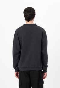 Dark gray sweatshirt with a relaxed fit, featuring a ribbed collar and cuffs, and a textured fabric. No visible logos or patterns.