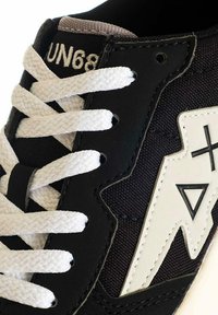 Sneaker nera con una tomaia in tessuto testurizzato, lacci bianchi e un audace design di un fulmine bianco sul lato.