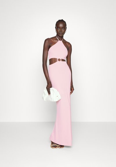 Vestido halter rosa claro com recorte na cintura, apresentando um detalhe circular. A modelo segura uma bolsa branca e usa sandálias douradas com tiras.