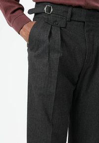 Donkergrijze, gestructureerde broek met een getailleerde pasvorm, voorzien van voorplooien, zijzakken en een riem met een zilveren gespsluiting.