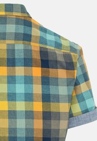 Vue arrière d'une chemise à manches courtes à carreaux avec des carrés bleus, jaunes et verts et des poignets pliés sur un fond clair.