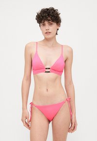 Roze bikini set met een driehoekige top met verstelbare bandjes en een zwarte hardware detail, gecombineerd met bikinibroekjes met striksluiting aan de zijkant.