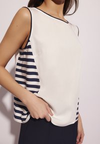 Top bez rękawów, z gładkim białym przodem i bokami w granatowo-białe paski, wykonany z lekkiego materiału o luźnym kroju.
