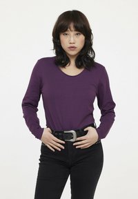 Chemise à manches longues violette avec un col rond, portée avec un pantalon noir et une ceinture noire texturée avec une boucle en argent.