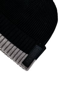 Gorro de punto negro con un puño acanalado gris. Presenta una superficie texturizada y una etiqueta rectangular negra en el lateral.