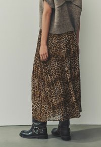 Kjole med leopardmønster og plisseringer lavet af letvægtig stof, parret med sorte ankelstøvler med strap og spænde detaljer.