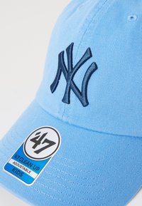 Căciulă de baseball bleu deschis, cu logo-ul NY brodat în albastru închis. Are o coamă curbă și o etichetă care spune "47 CLEAN UP ADJUSTABLE KIDS."