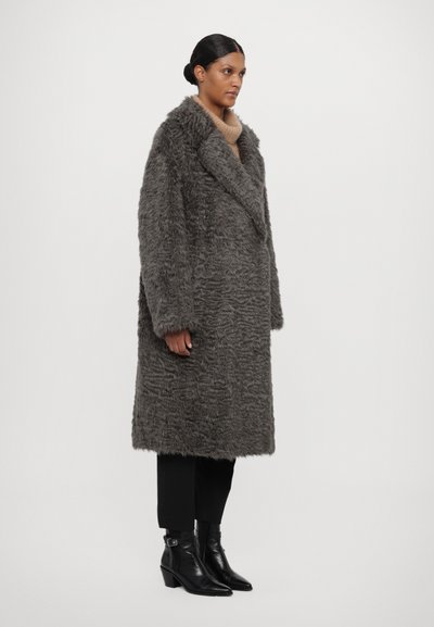 Pilkas dirbtinio kailio paltas su plačiu apykakle ir tekstūruota paviršiumi. Dėvimas ant juodų kelnių ir kulkšninių botų, po juo - neutralaus atspalvio megztinis.