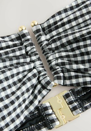 Črno-bele gingham tkanine z nabranimi odseki, ki imajo zlat ton kovinskega spona in črne poudarke, kar ustvarja teksturiran in strukturiran dizajn.