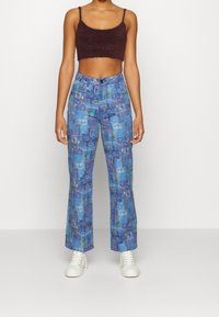 Pantalon bleu à motif avec un collage d'images, conçu avec une coupe évasée et des poches avant, assorti à un court haut marron pelucheux et des baskets blanches.