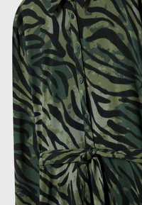 Vestito camicia a strisce zebra verde e nera, dotato di colletto, patta dei bottoni e una cintura in tessuto, realizzato in materiale leggero e liscio.