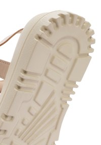 Semelle en caoutchouc beige avec un motif de grip texturé et des bords nervurés ; présente des triangles et des rectangles pour l'adhérence et le soutien.