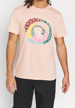 Kurzärmliges, hellrosa T-Shirt aus Baumwolle, mit einem kreisförmigen Grafikdesign, das mehrfarbigen Text und Silhouetten von zwei Wanderern in der Mitte zeigt.