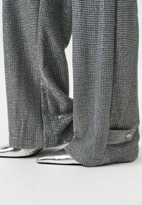 Brede, gestructureerde broeken in metallic zilver met een horizontaal streepjespatroon, gecombineerd met puntige zilveren ballerina's. Bevat een knopdetail op de broek.