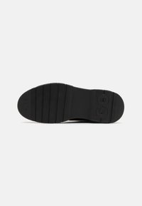 Semelle de chaussure en caoutchouc noir avec des rainures horizontales, une prise texturée et des logos de marque embossés près des zones du talon et des orteils.