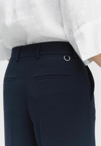 Pantalons ajustés bleu marine avec une texture lisse, comportant un accent en métal argenté à l'arrière et deux poches arrière sans couture visible.