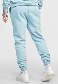 Světle modré tepláky s elastickými náplety na kotnících, s jemnou texturou. Nosit s bílými teniskami a viditelnými bílými kotníkovými ponožkami.