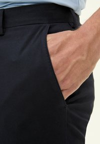 Mörkblå byxor gjorda av ett glatt tyg, med en sidoficka och en figursydd midja. Tyget verkar lätt och har en ren finish.