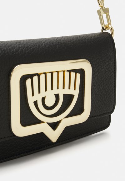 Borsa a tracolla in pelle nera con un design a occhio in metallo dorato in evidenza nella parte anteriore, con una finitura testurizzata e chiusura a patta.