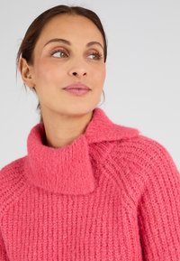 Maglione lavorato a maglia di un brillante colore rosa, con colletto alto ripiegato, texture a costine e dettagli unici lungo le spalle.
