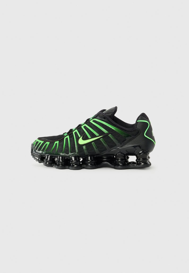 Black athletic shoe with green accents, featuring a textured upper, supportive design, and a distinctive chunky outsole with rounded elements.