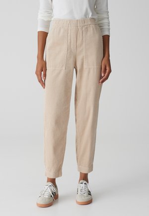 Beige corduroy broek met een losse pasvorm, voorzien van een elastische tailleband en twee steekzakken, gecombineerd met lichte sneakers.