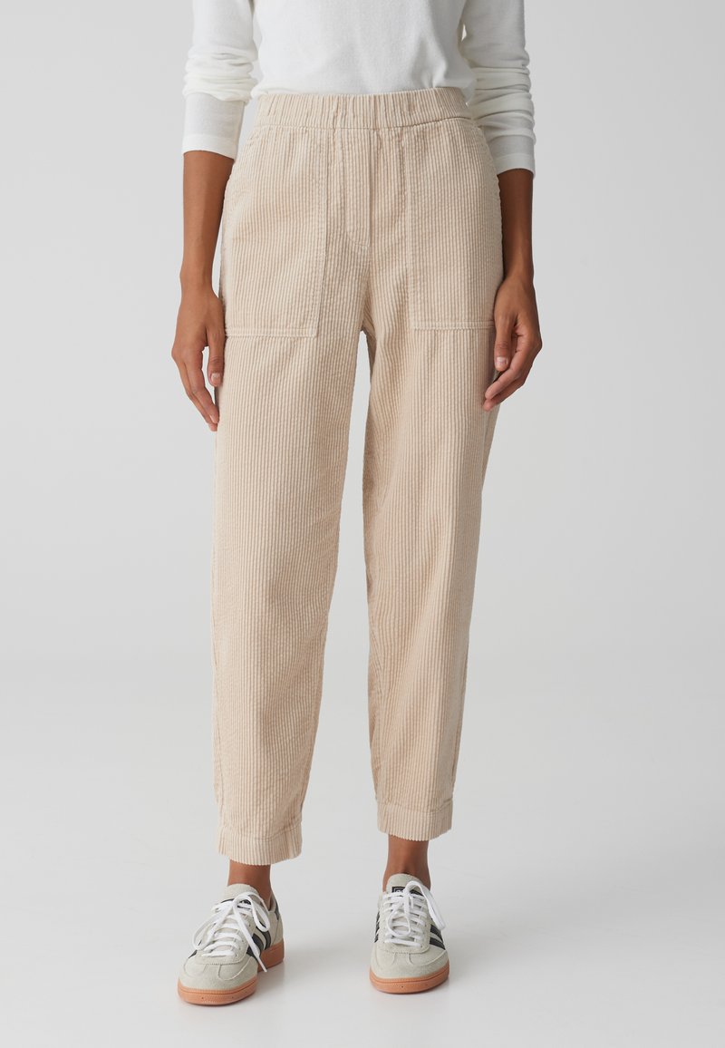 Beige corduroy broek met een losse pasvorm, voorzien van een elastische tailleband en twee steekzakken, gecombineerd met lichte sneakers.
