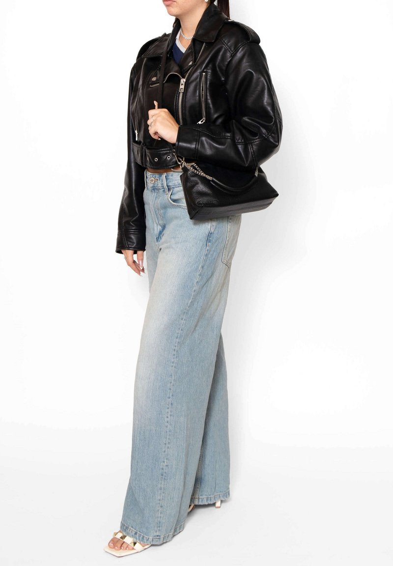 Zwarte leren cropped jack met ritsen, gecombineerd met lichtblauwe wijde jeans. Zwarte handtas met kettinghengsel, witte hakken.