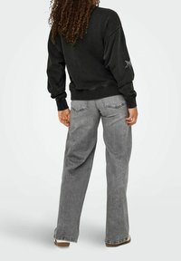 Sweatshirt noir avec poignets côtelés, associé à un jean gris à jambes larges. Détail notable : accent étoile argentée sur la manche.